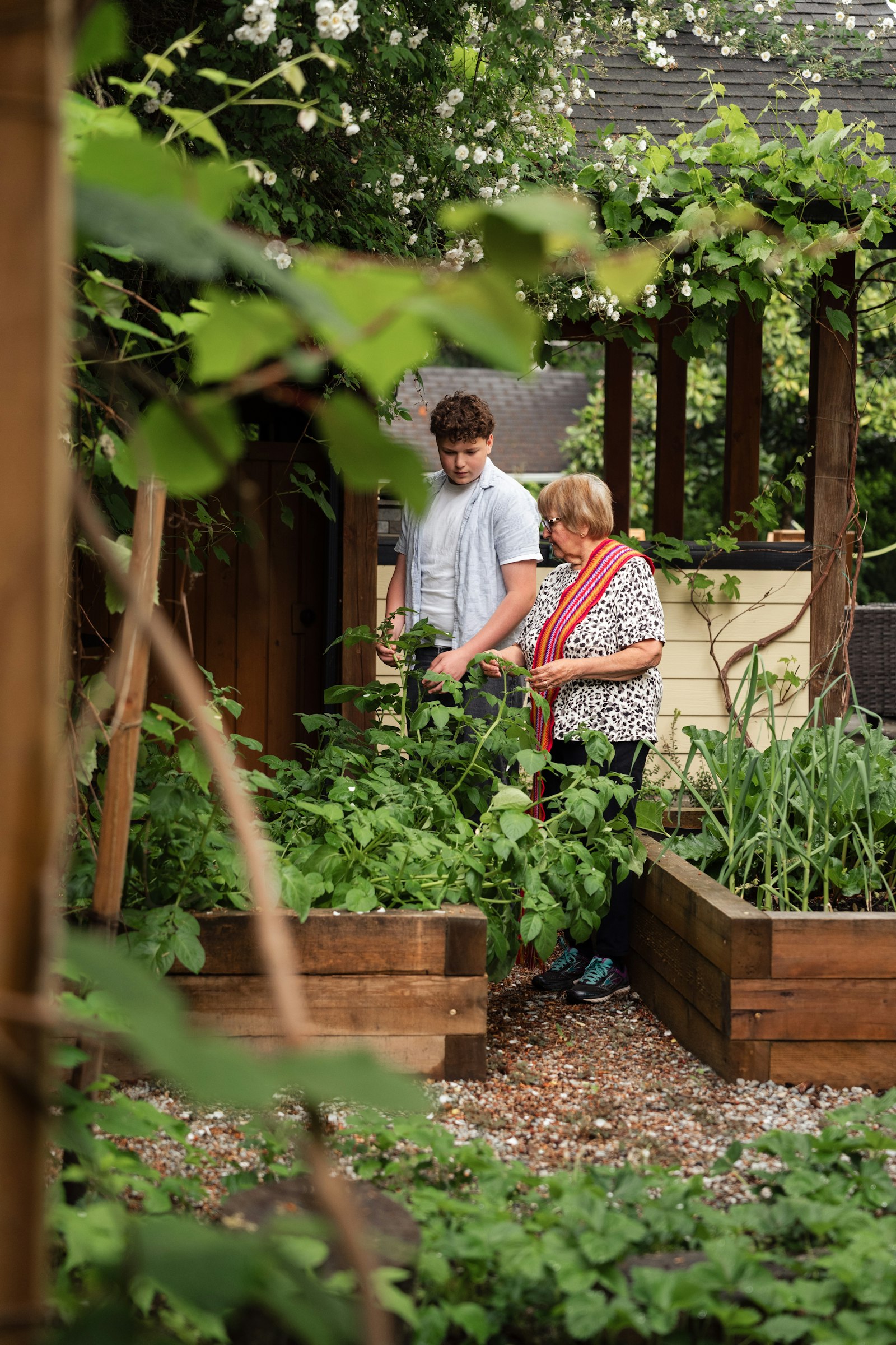 A young person and an older woman tending plants in a raised garden bed